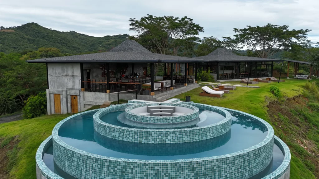 Moderna villa de arquitectura abierta con piscina circular infinita de varios niveles, tumbonas y un exuberante paisaje verde: un entorno ideal para el bienestar de lujo o uno de los mejores retiros de yoga frente a colinas boscosas.