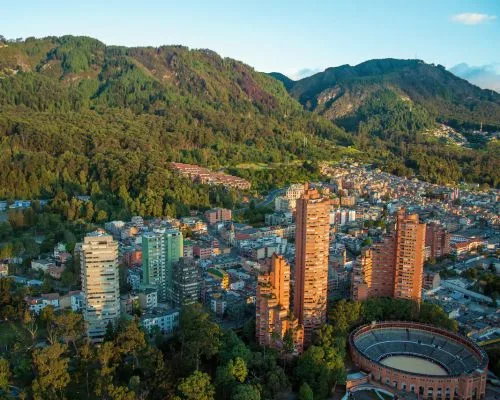 Smiling woman in foreground with an aerial view of a city known for its medical tourism, tall buildings, and green mountains in the background.
