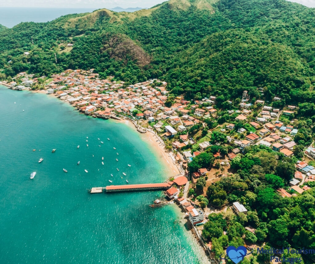 Aerial view of a coastal town in Panama with houses, a pier, docked boats, and green hills surrounding turquoise water—one of the top Tourist Attractions Panama has to offer.