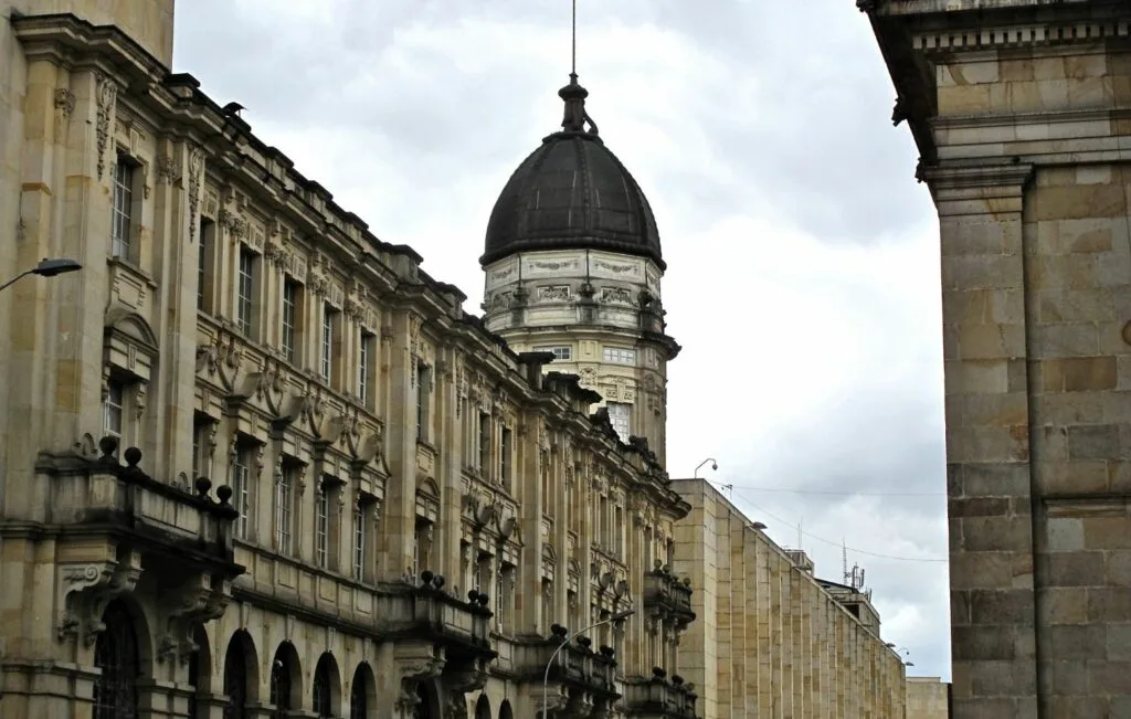 Ubicado bajo un cielo nublado, este histórico edificio colombiano ostenta una fachada ornamentada y una cúpula central, captada desde un ángulo bajo, testimonio de la belleza arquitectónica que complementa el creciente atractivo del país como destino de turismo médico.