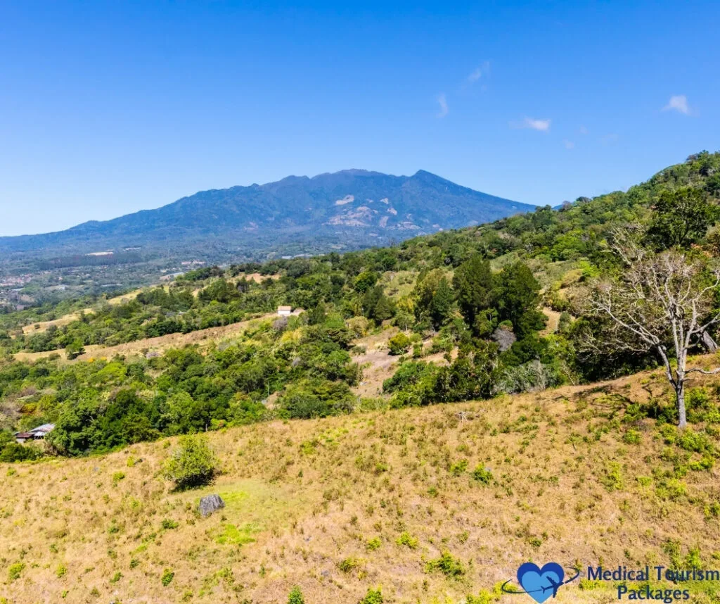 Un paisaje escénico con colinas cubiertas de hierba y árboles dispersos en primer plano, y una gran montaña boscosa bajo un cielo azul claro en el fondo, perfecto para aquellos que buscan inspiración para viajar a Panamá o que buscan atracciones turísticas únicas que ofrece Panamá.