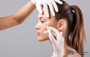 A person receives a Botox procedure in the side of their face, assisted by two gloved hands against a plain background.