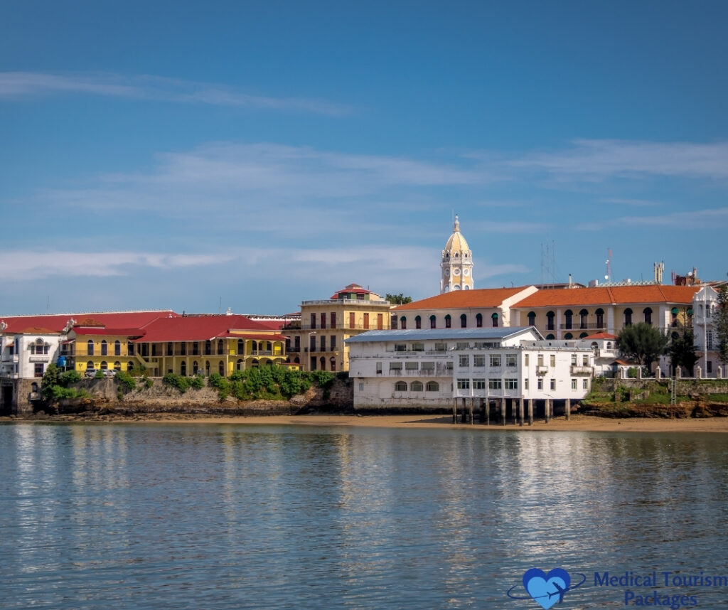 Waterfront view of colorful colonial buildings with red roofs and a clock tower under a blue sky, reflected in calm water—a stunning scene showcasing top tourist attractions Panama offers for unforgettable Panama tourism experiences.
