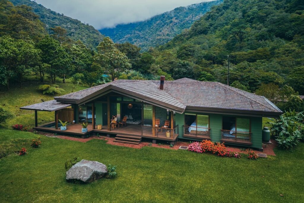 Una moderna casa de una sola planta con grandes ventanales se asienta en un exuberante y verde paisaje montañoso: una escapada a Costa Rica ideal para viajeros por motivos médicos o para quienes busquen retiros de bienestar entre árboles y flores de colores.