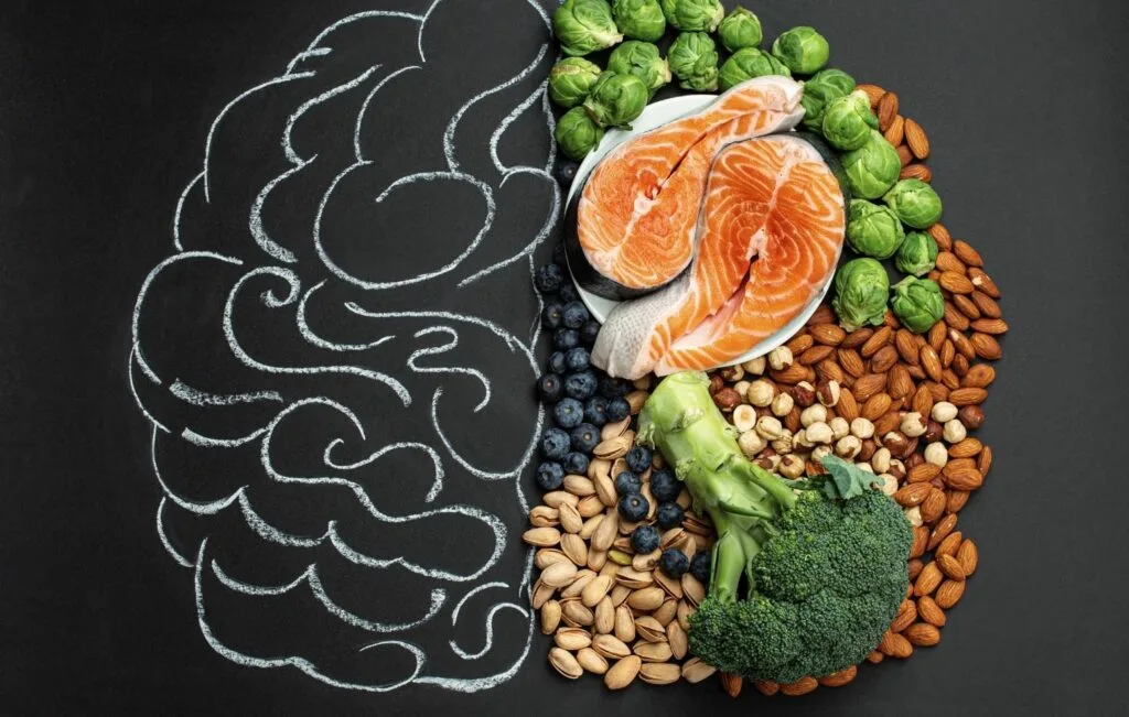 Various healthy foods, including salmon, nuts, vegetables, and berries, are arranged on a surface next to a chalk drawing of a brain—perfect choices for stress relief after wellness retreats or a rejuvenating vacation.