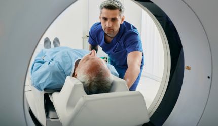 A medical professional supports an older patient lying on a table as he enters a CT or MRI scanner, highlighting the importance of safeguarding health through preventative imaging.