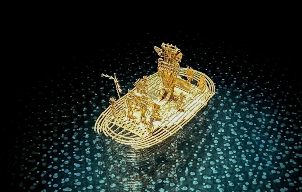 Golden raft sculpture on dark display background with dotted light reflections, inspired by Colombian culture.