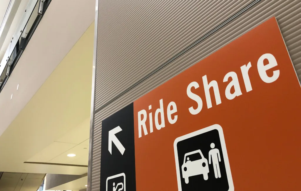 Una señal de "Ride Share" con una flecha apuntando a la izquierda está colocada en una pared dentro de un edificio, guiando a los viajeros a la zona de recogida de vehículos compartidos. Siga los consejos esenciales para llegar sin problemas a su destino.