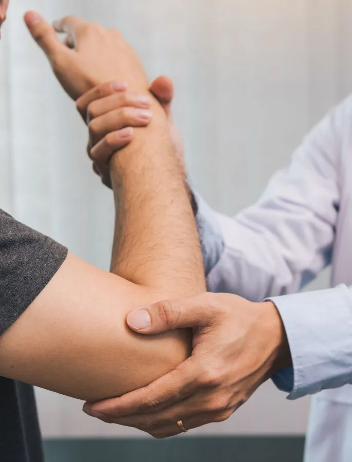 A healthcare professional holds and examines a person's bent arm at the elbow and wrist, highlighting affordable orthopedic surgeries available in Latin America.