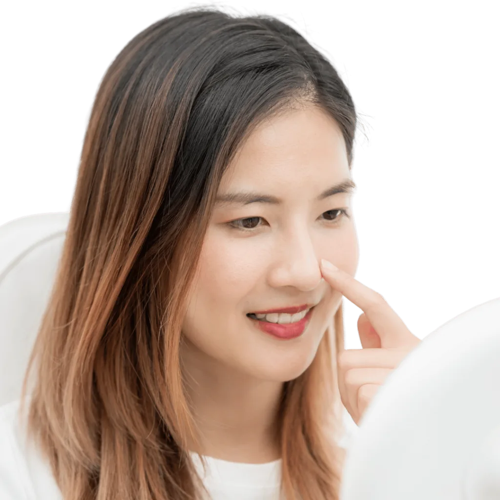 A woman smiling and touching her nose while looking at a mirror.