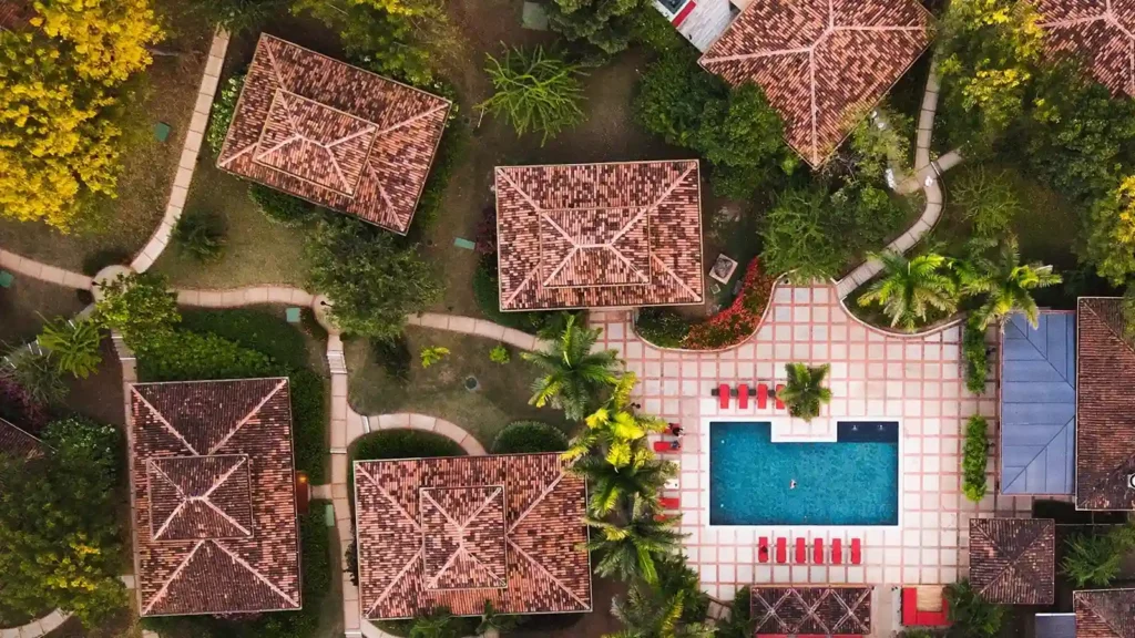 Vista aérea de una zona residencial de Costa Rica con casas de tejados de tejas, un patio central, piscina y frondosos árboles, ideal para retiros de bienestar o viajeros médicos en busca de relajación y comodidad.
