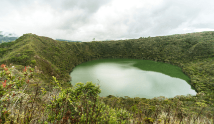 A circular green lake surrounded by dense forest and hills under a cloudy sky, offering a perfect escape for those seeking balance and wellness in nature.