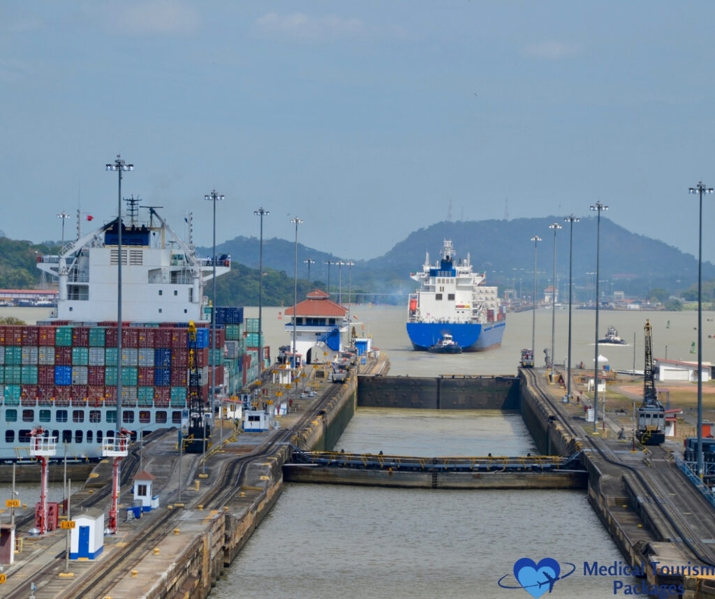 Large cargo ships pass through the locks of the Panama Canal, with containers stacked on decks and a hilly landscape in the background—one of the top things to do in Panama and a must-see among Panama tourist attractions.