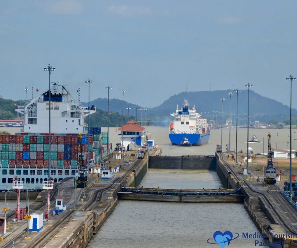 Grandes buques de carga atraviesan las esclusas del Canal de Panamá, con contenedores apilados en las cubiertas y un paisaje montañoso de fondo: una de las mejores cosas que hacer en Panamá y una visita obligada entre las atracciones turísticas de Panamá.